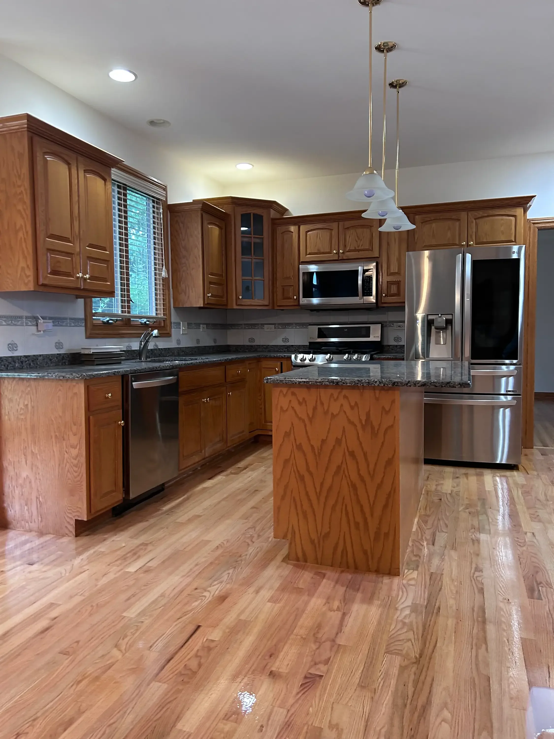 Warm oak hardwood flooring installed in kitchen with wood cabinets and granite counters