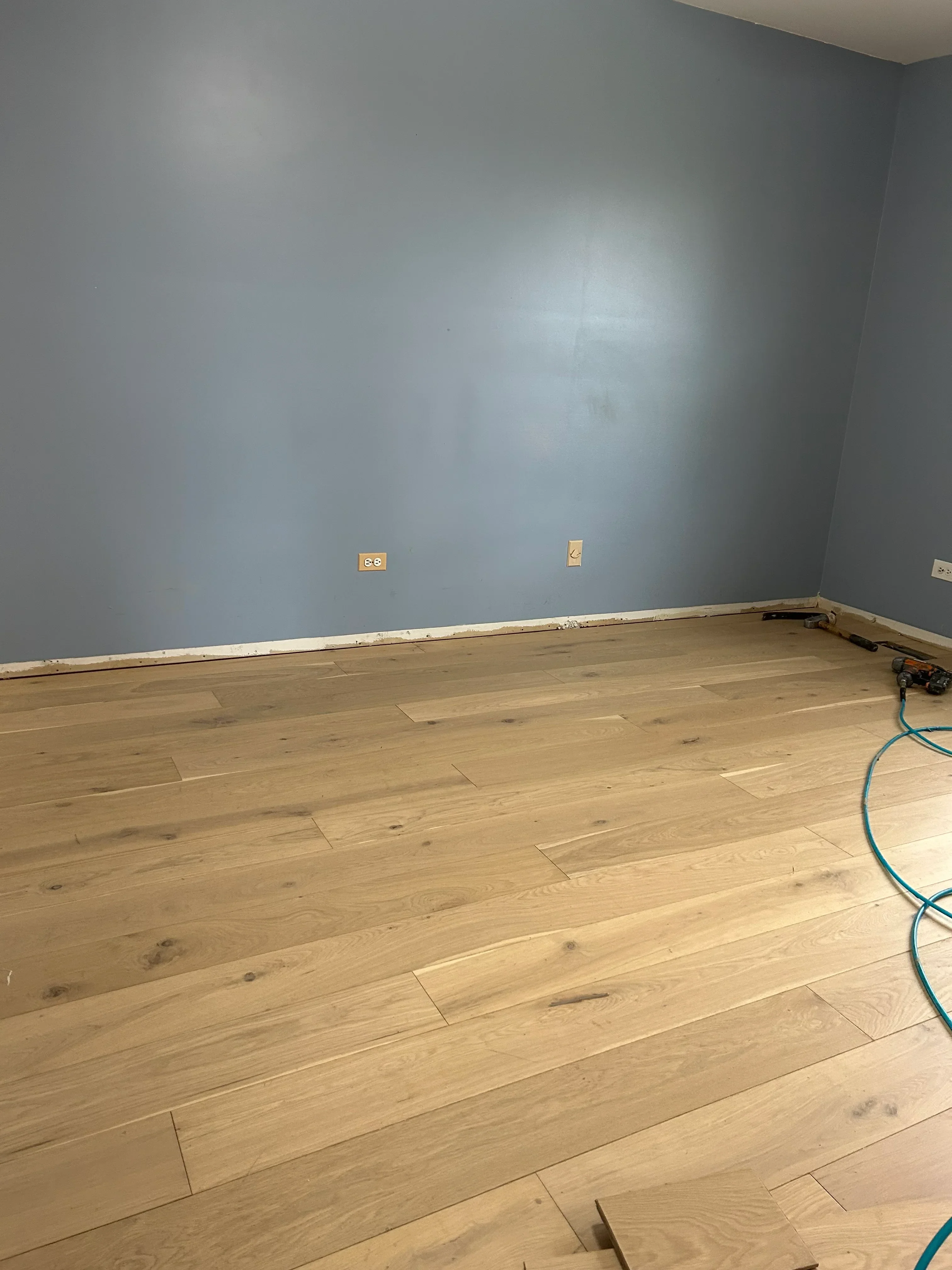 Wide-plank oak hardwood flooring installation with natural finish and baseboard trim